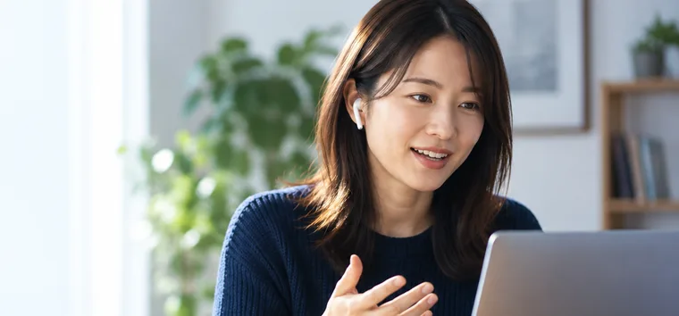 イヤホンを着けてノートパソコンでオンライン英語学習をする女性